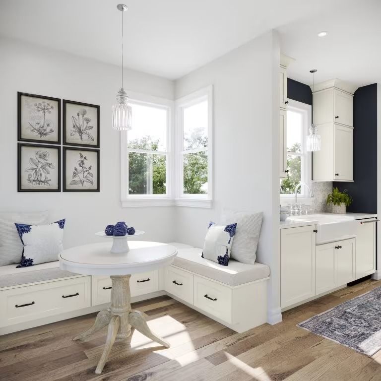 Bright white breakfast nook with built-in benches, round table, and floral wall art beside a kitchen.