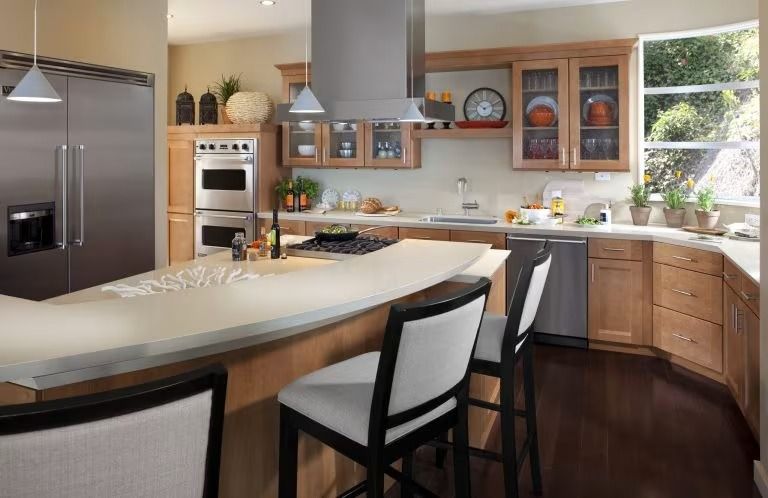 Modern kitchen with curved island, stainless steel appliances, wood cabinets, and large window by sink
