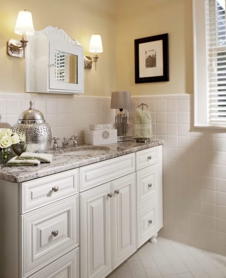 Bright bathroom vanity with white cabinets, granite countertop, wall sconces, and a window.