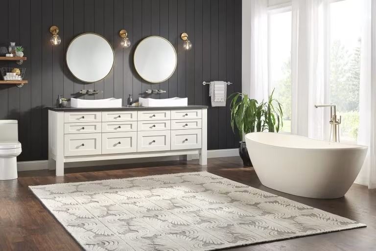 Modern bathroom with double vanity, round mirrors, freestanding tub, dark walls, and a patterned rug.