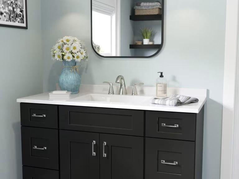 Modern bathroom vanity with black cabinets, white countertop, mirror, and blue vase of flowers