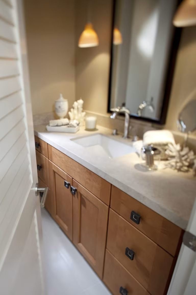 Modern bathroom vanity with wood cabinets, white countertop, sink, mirror, and warm pendant lighting.