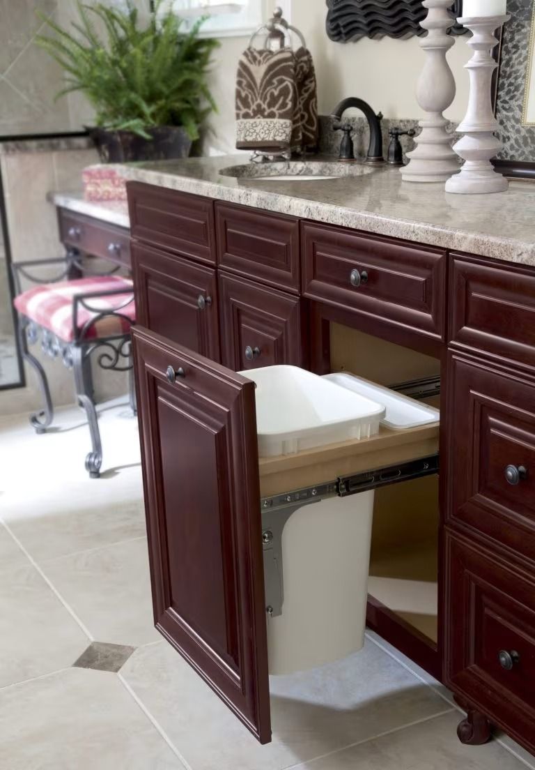 Open bathroom vanity cabinet with a pull-out trash bin under a dark wood countertop