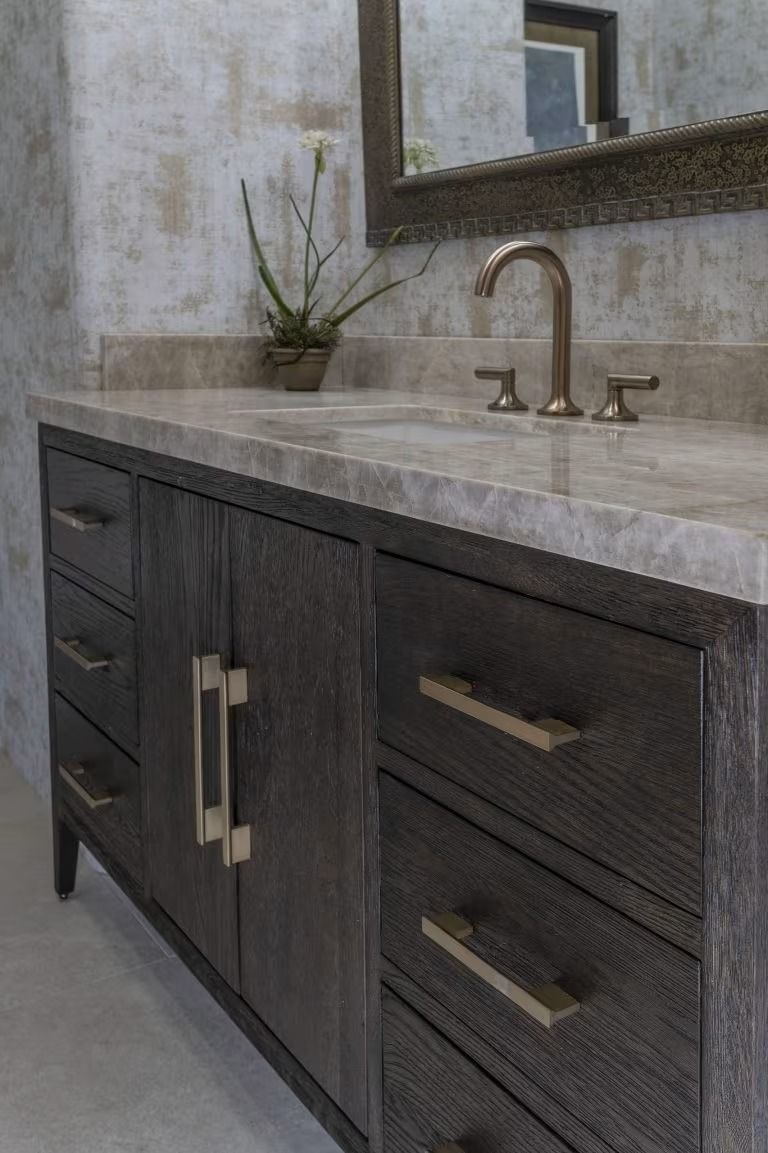 Dark wood bathroom vanity with marble countertop, sink, and brass faucet beneath a mirror