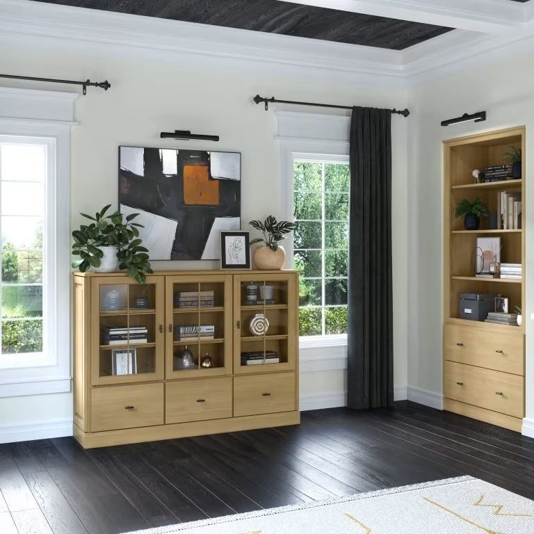 Modern living room with light wood cabinets, dark wood floor, framed art, and tall windows with gray curtains