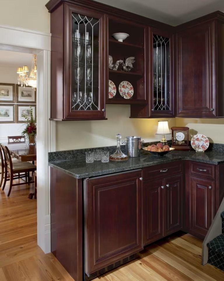 Dark cherry kitchen corner cabinets with glass doors and granite countertop in a dining area