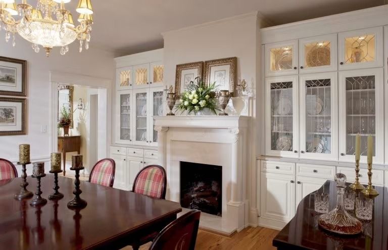 Elegant dining room with white fireplace, dark wood table, chandeliers, and glass-front cabinets