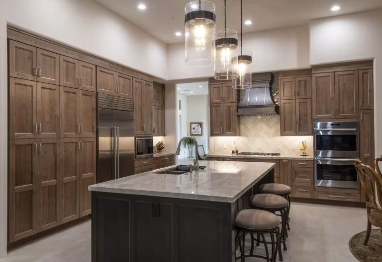 Modern kitchen with dark wood cabinets, large island, pendant lights, and stainless steel appliances.