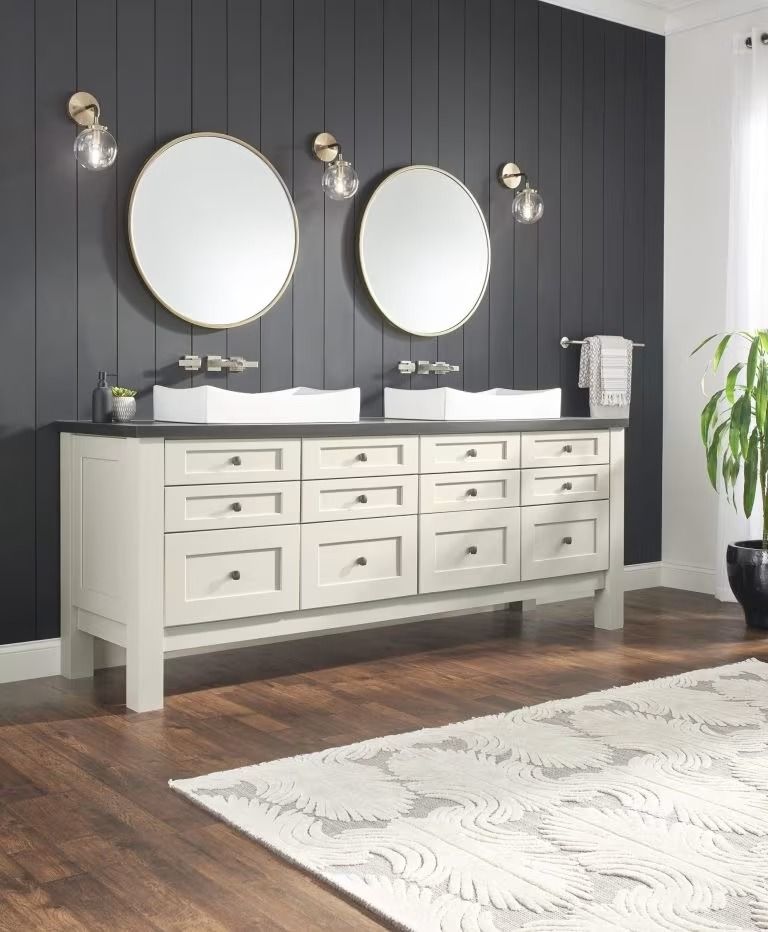 Modern bathroom with double vanity, round mirrors, dark paneled wall, and white rug on wooden floor