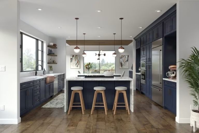 Modern kitchen with dark blue cabinets, wood floors, island stools, and large windows overlooking greenery