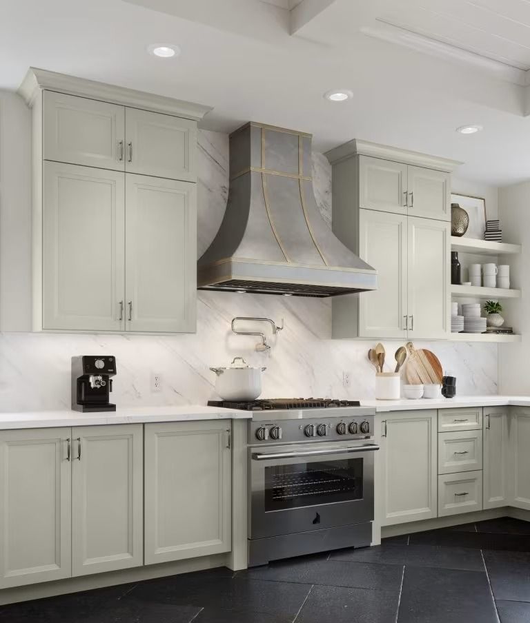 Modern kitchen with light gray cabinets, stainless range hood, white countertops, and black tile floor