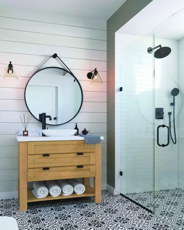 Modern bathroom with round mirror, wooden vanity, and glass shower with black fixtures.
