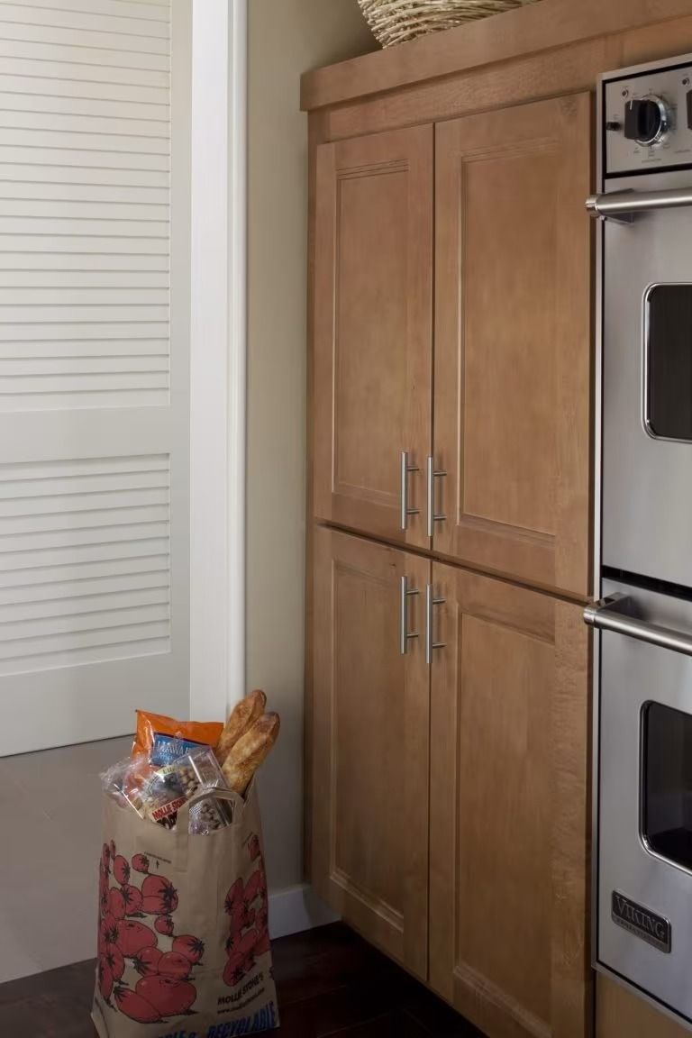 Kitchen corner with wooden cabinets, built-in oven, and a grocery bag on the floor.