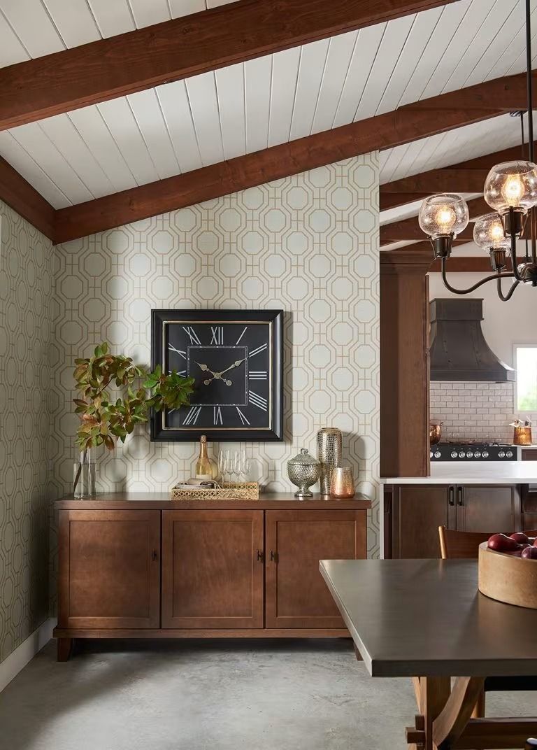 Dining room with wood sideboard, wall clock, patterned wallpaper, and a dark table under exposed beams.