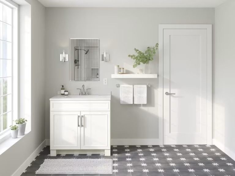 Bright bathroom with white vanity, wall mirror, shelf, and patterned gray floor tiles.