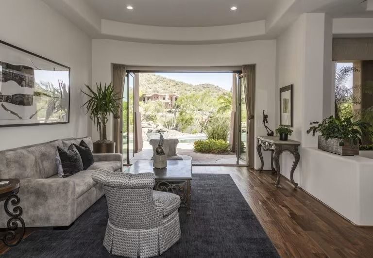 Modern living room with gray sectional, black rug, and open glass doors to a sunny patio