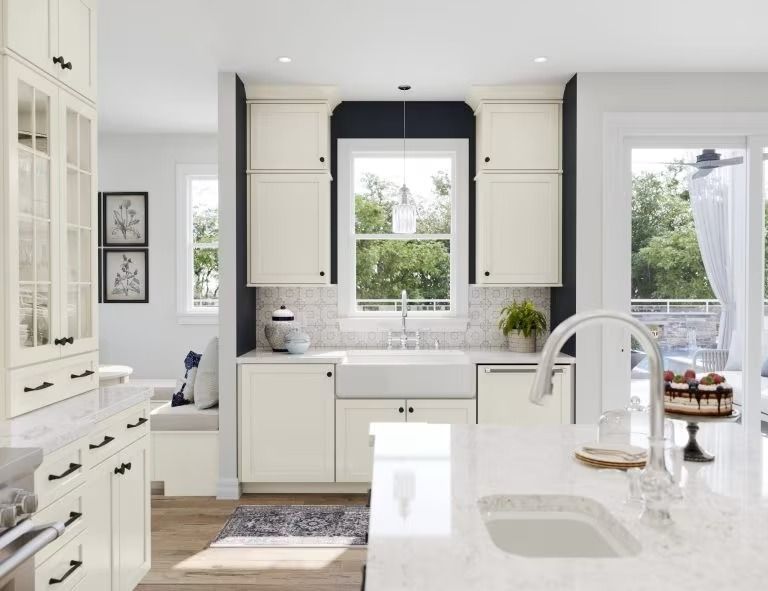 Bright white modern kitchen with island, farmhouse sink, and black-trimmed window above the counter.