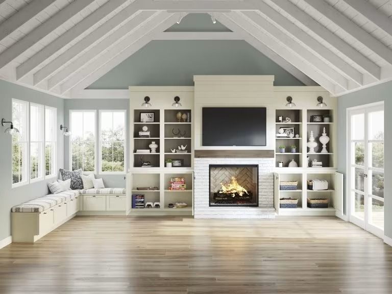 Bright living room with vaulted ceiling, fireplace, built-in shelves, windows, and light wood floors