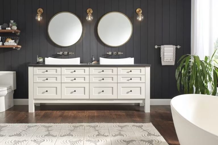 Modern double vanity bathroom with white sinks, round mirrors, and dark paneled walls