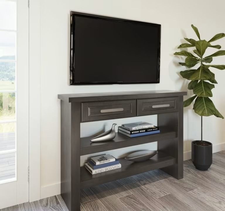 Wall-mounted TV above a dark gray console table with books and decor in a bright room.