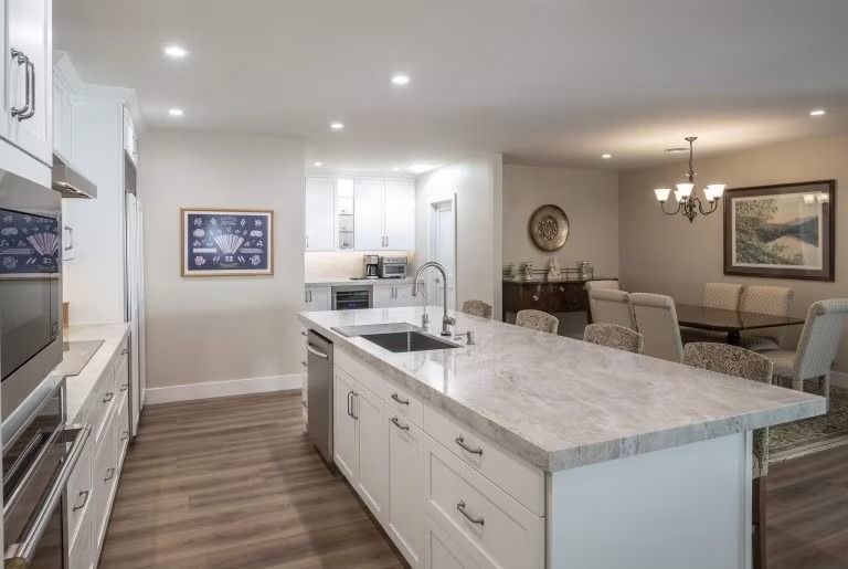 Bright modern kitchen with island, white cabinets, wood floors, and open dining area