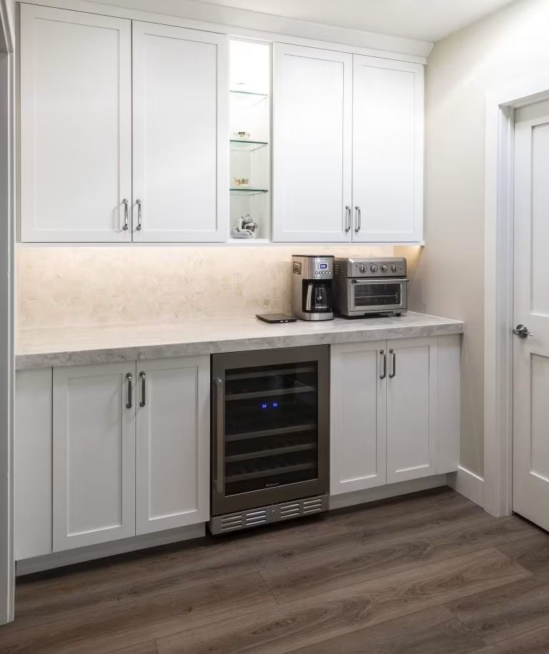 Modern white kitchen with built-in cabinets, countertop appliances, and a stainless wine fridge.