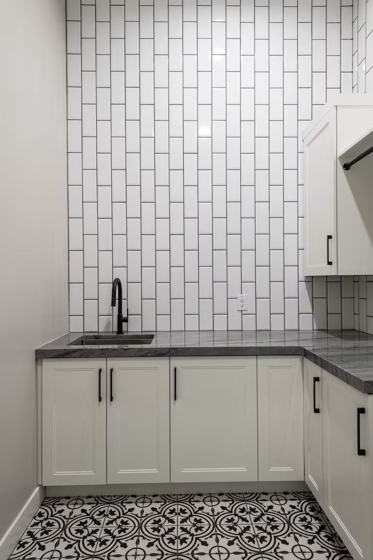 Modern kitchen with white cabinets, gray countertop, subway tile backsplash, and patterned black-and-white floor.