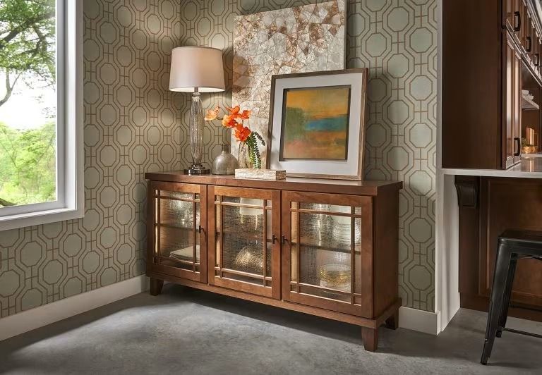 Modern living room corner with wooden sideboard, lamp, framed art, and patterned wallpaper