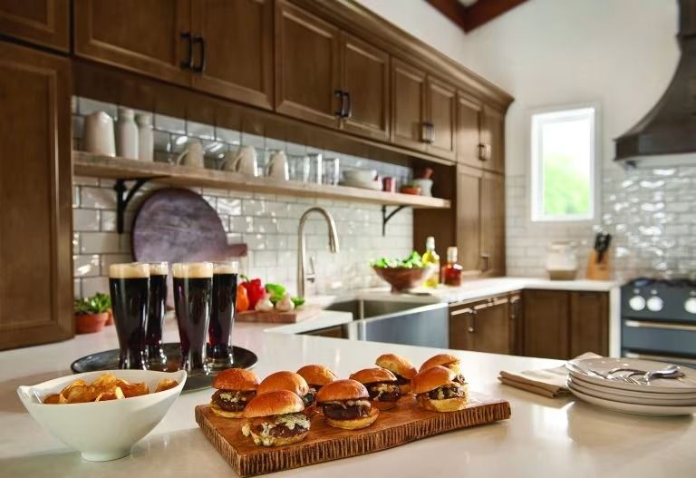 Modern kitchen counter with burgers, snacks, wine glasses, and a bowl of food on a tray