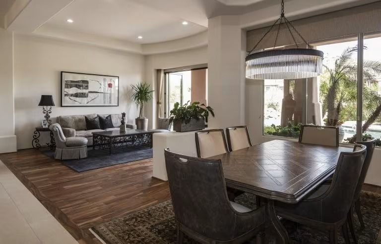 Bright open-concept living and dining room with wood floors, gray sofa, dark dining table, and large windows