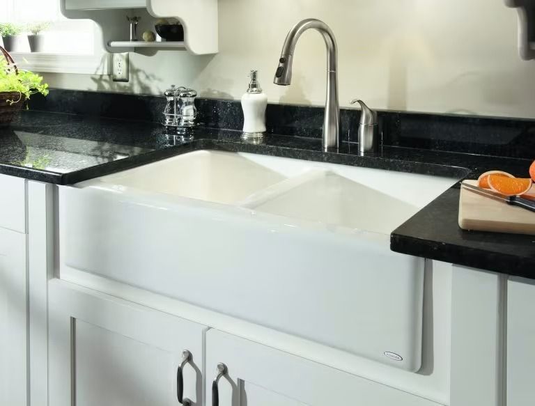 Modern white kitchen sink with black granite countertop and chrome faucet.