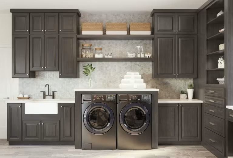 Modern laundry room with dark cabinets, stacked shelves, countertop sink, and two front-loading washers/dryers