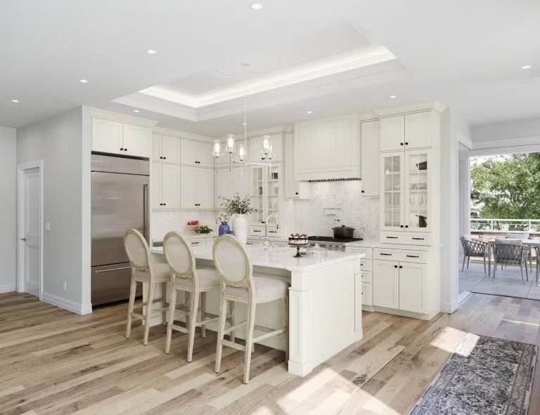 Bright modern white kitchen with island seating, stainless appliances, and open dining area