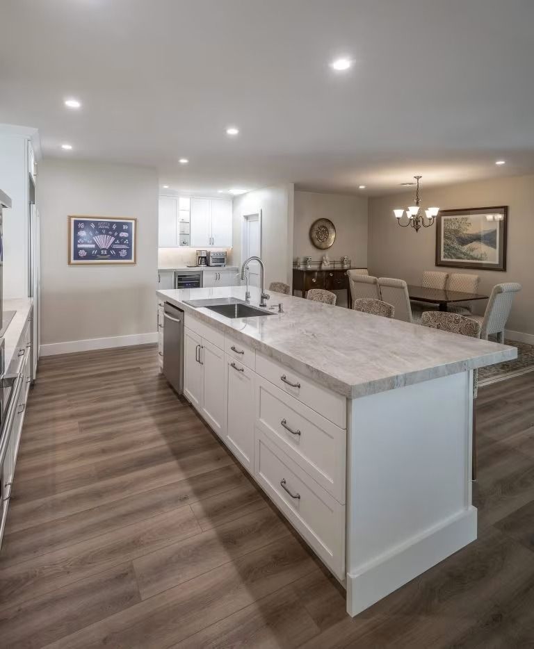 Bright open kitchen and dining area with large island, white cabinets, wood floors, and recessed lighting