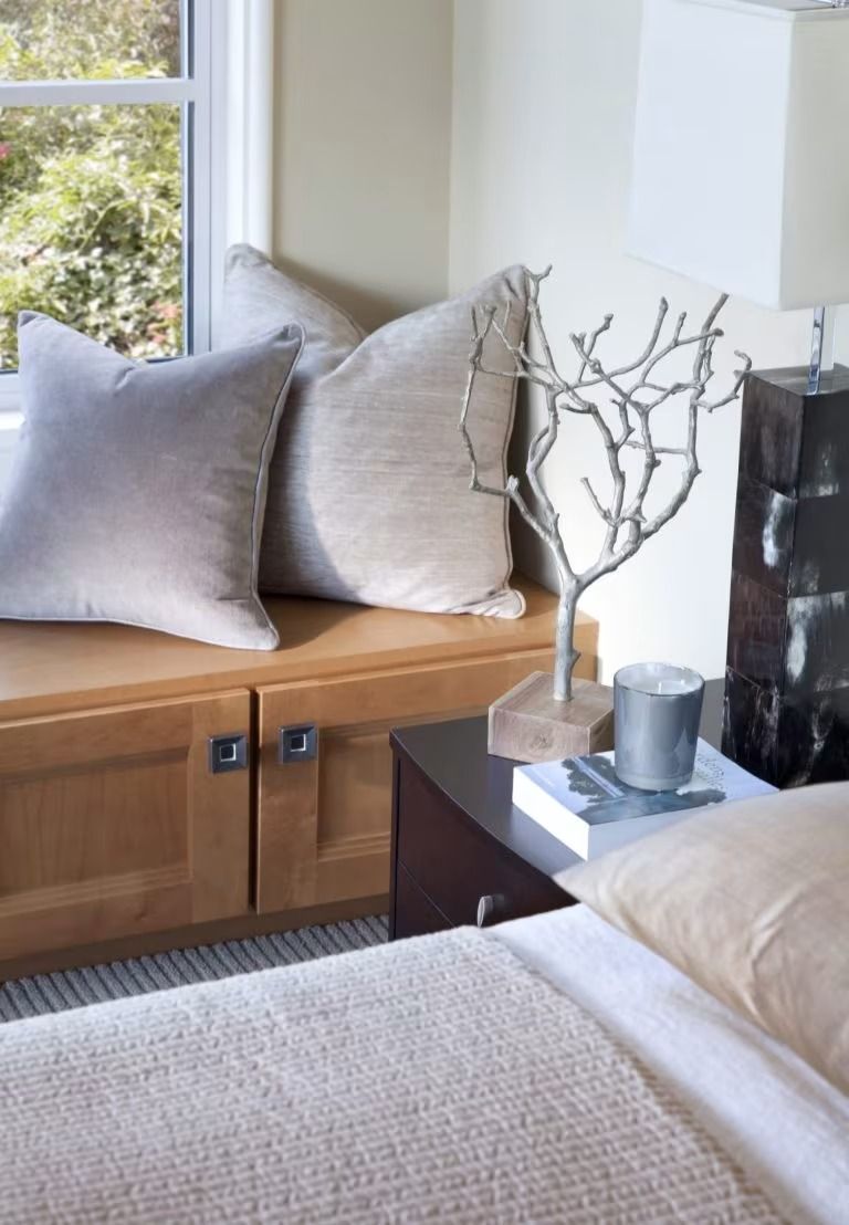 Cozy window nook with beige cushions, bedside table, and white lamp in a bright bedroom