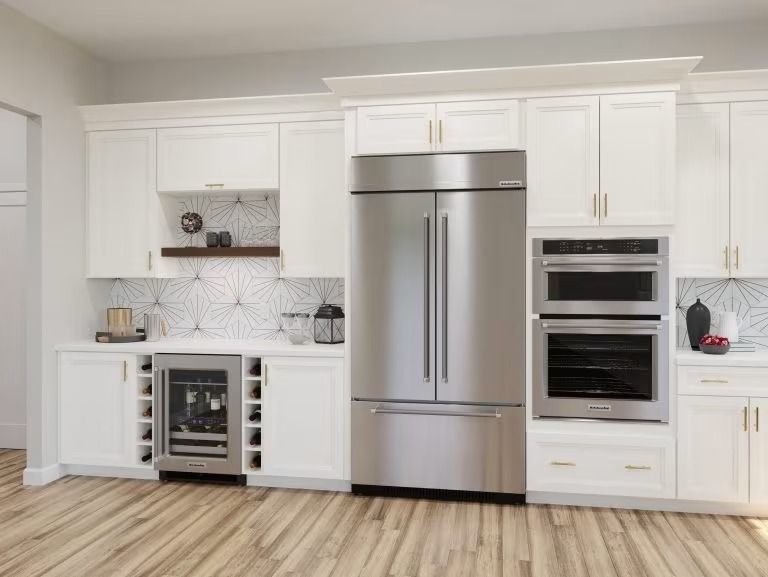 Modern white kitchen with stainless steel refrigerator, double ovens, and wood floor