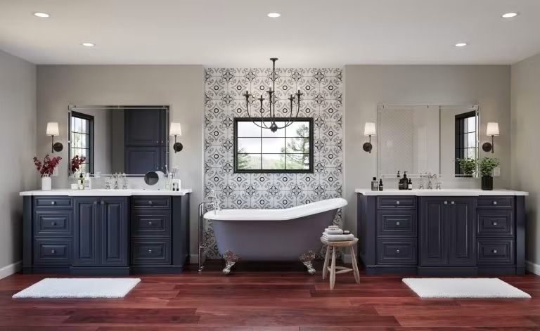 Symmetrical bathroom with double vanities, freestanding tub, patterned accent wall, and red wood floor