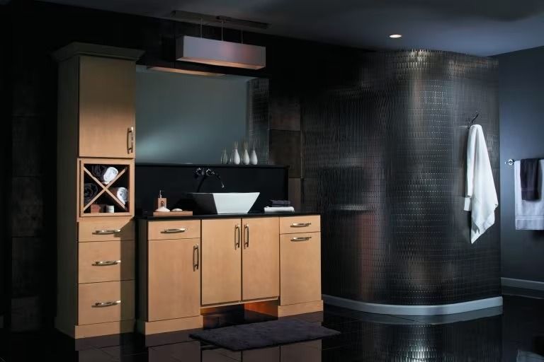 Modern bathroom vanity with light wood cabinets, black countertop, mirror, towel, and dark tiled walls