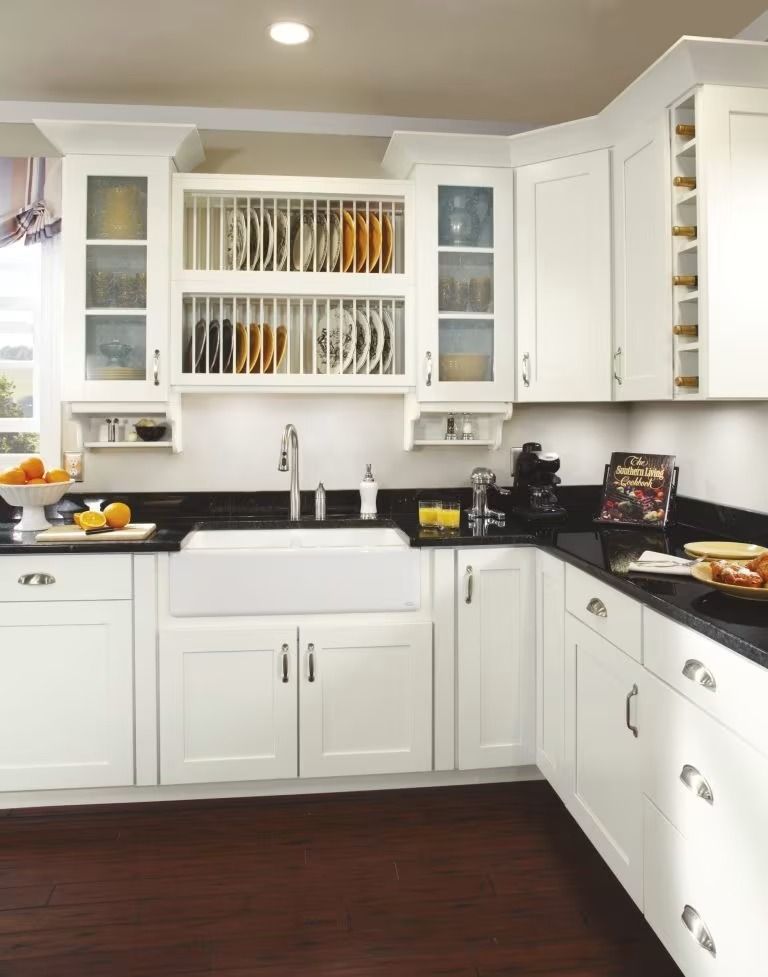 Bright white kitchen with black countertops, sink, cabinets, and a dark wood floor.