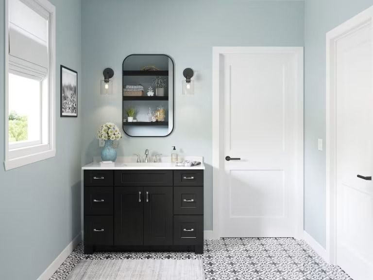 Bright bathroom with black vanity, round mirror, blue walls, and patterned floor tiles.