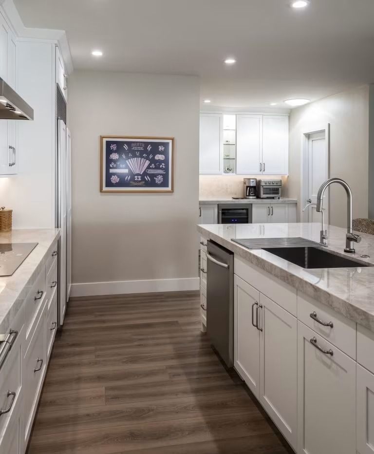 Modern white kitchen with island, marble counters, wood floors, and recessed lighting