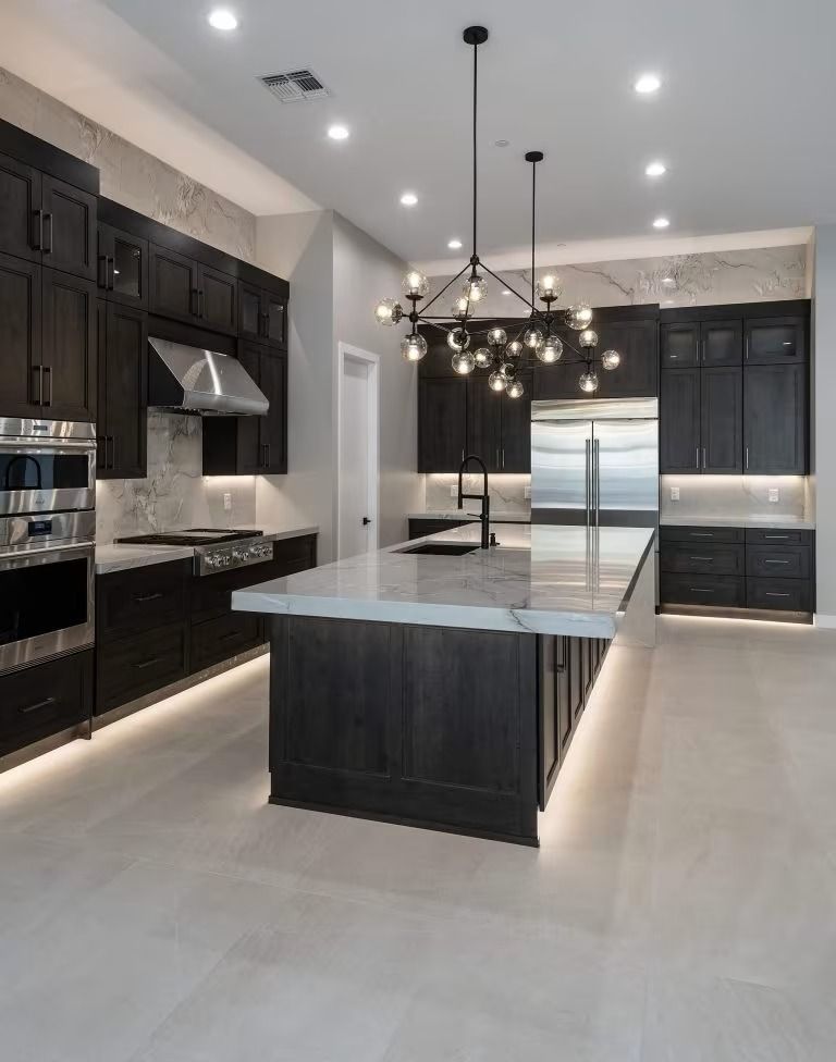 Modern luxury kitchen with dark cabinets, large island, pendant chandelier, and built-in stainless appliances.