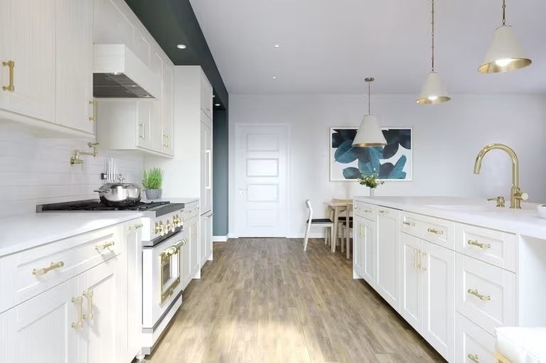 Bright white modern kitchen with island, gold fixtures, wood floor, and dining area in the background