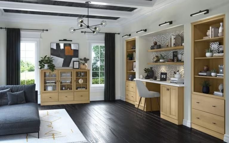 Bright modern living room with dark sofa, wood cabinets, desk nook, and large windows