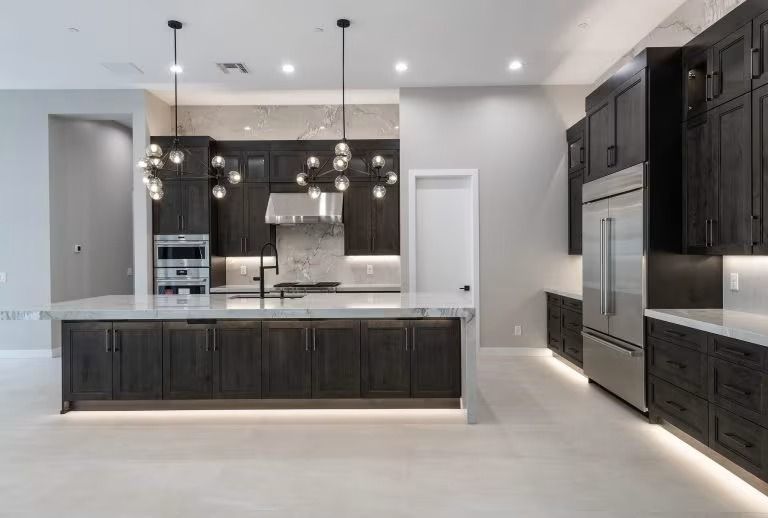 Modern kitchen with dark cabinets, white island, pendant lights, and stainless steel appliances