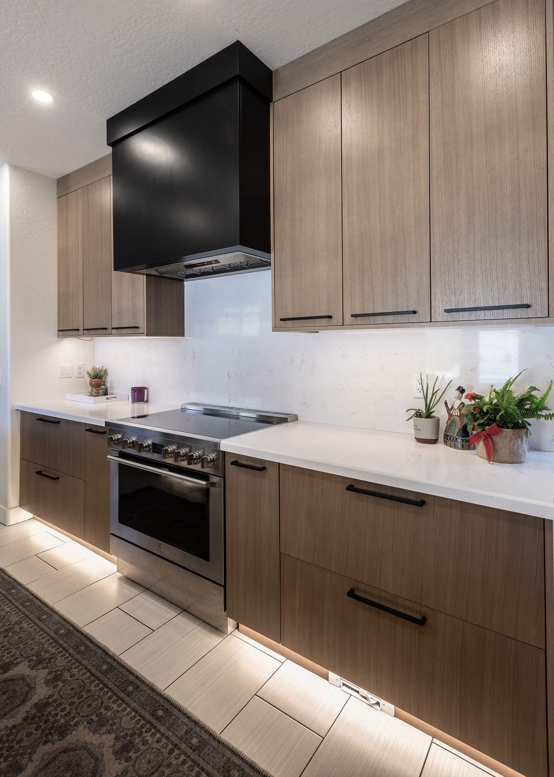 Modern kitchen with wood cabinets, black range hood, white countertops, and stove under recessed lighting