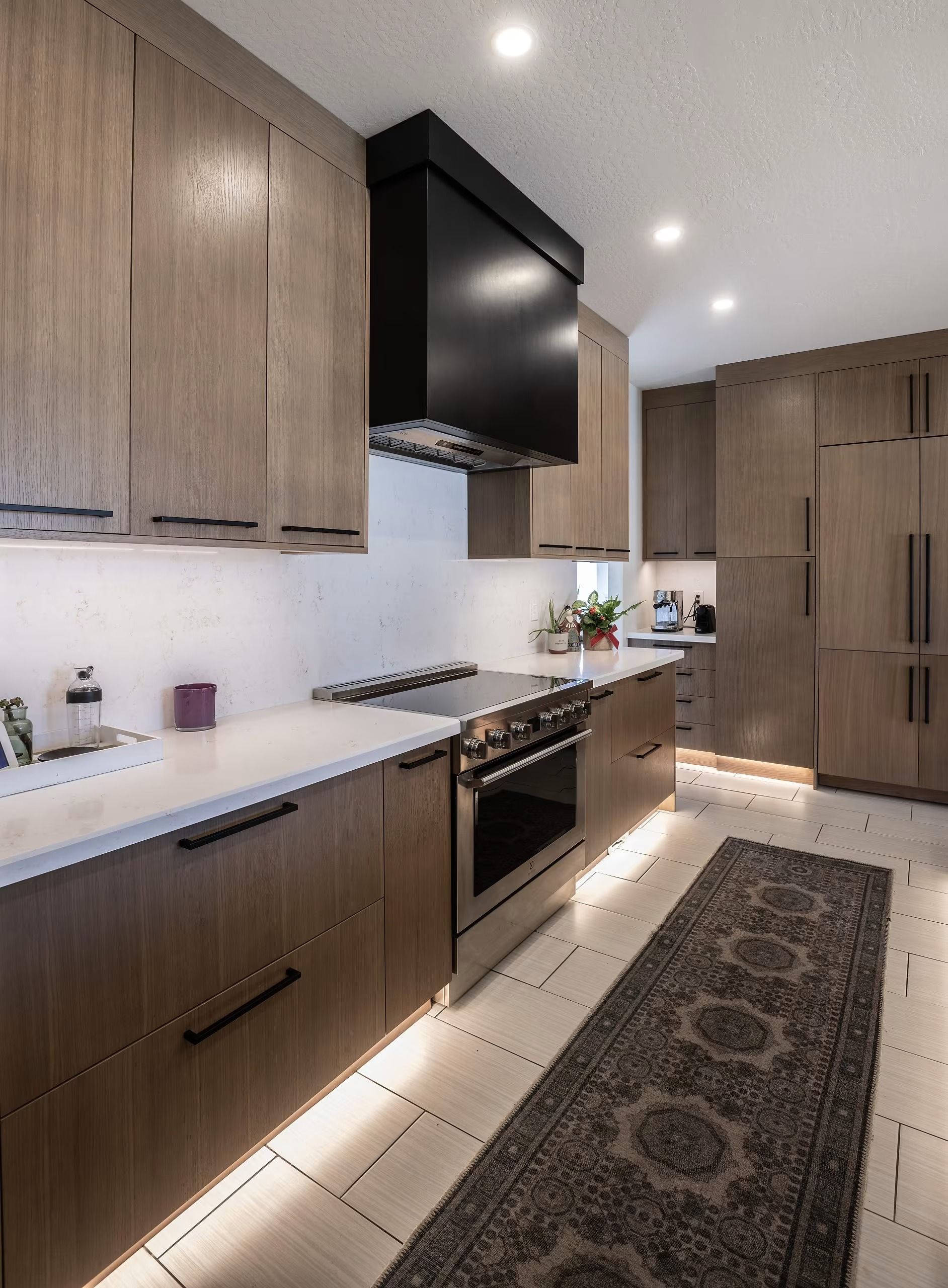 Modern kitchen with wood cabinets, white countertops, black range hood, and patterned runner rug.