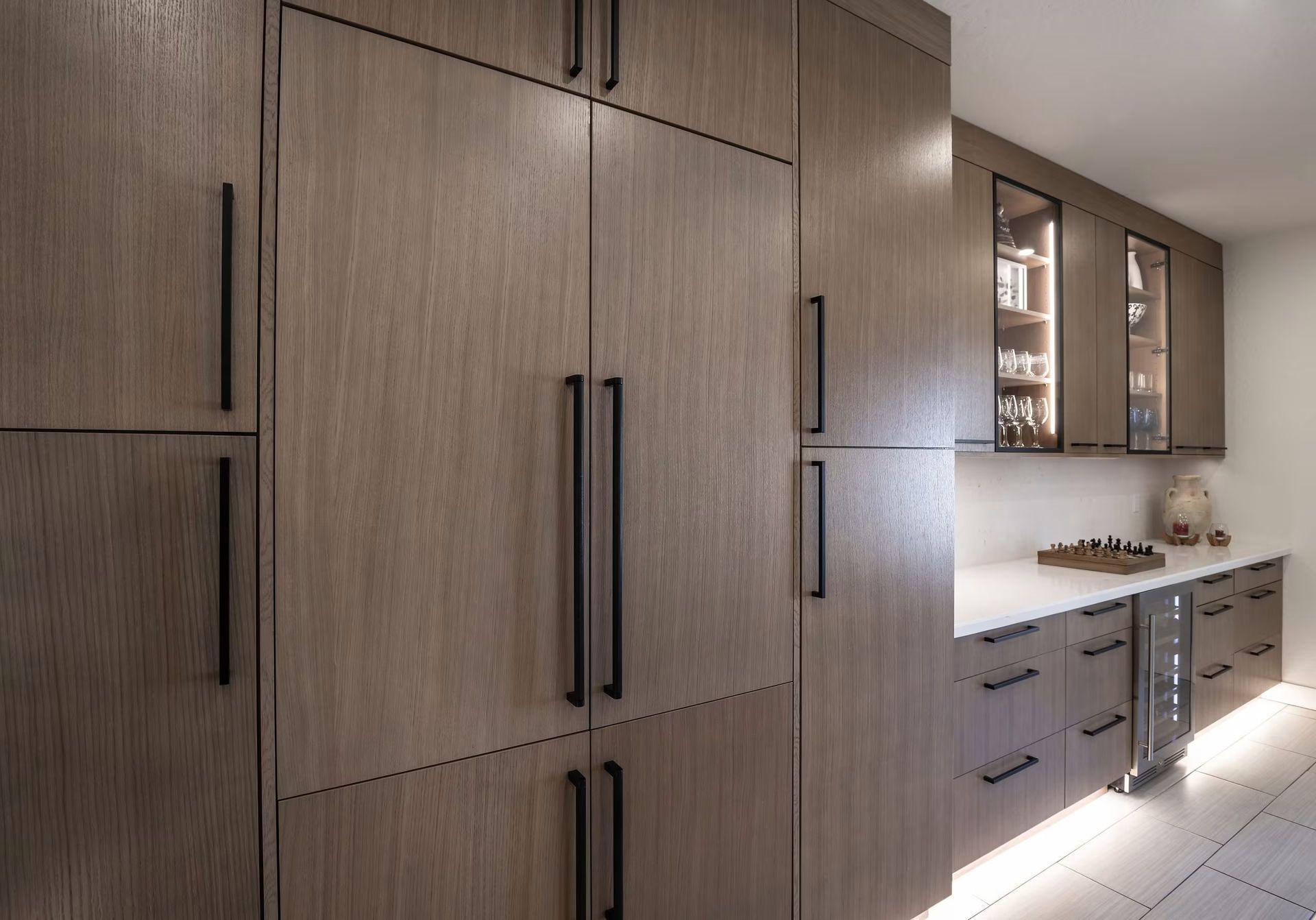 Modern kitchen with wood cabinets, black handles, white countertop, and tiled floor