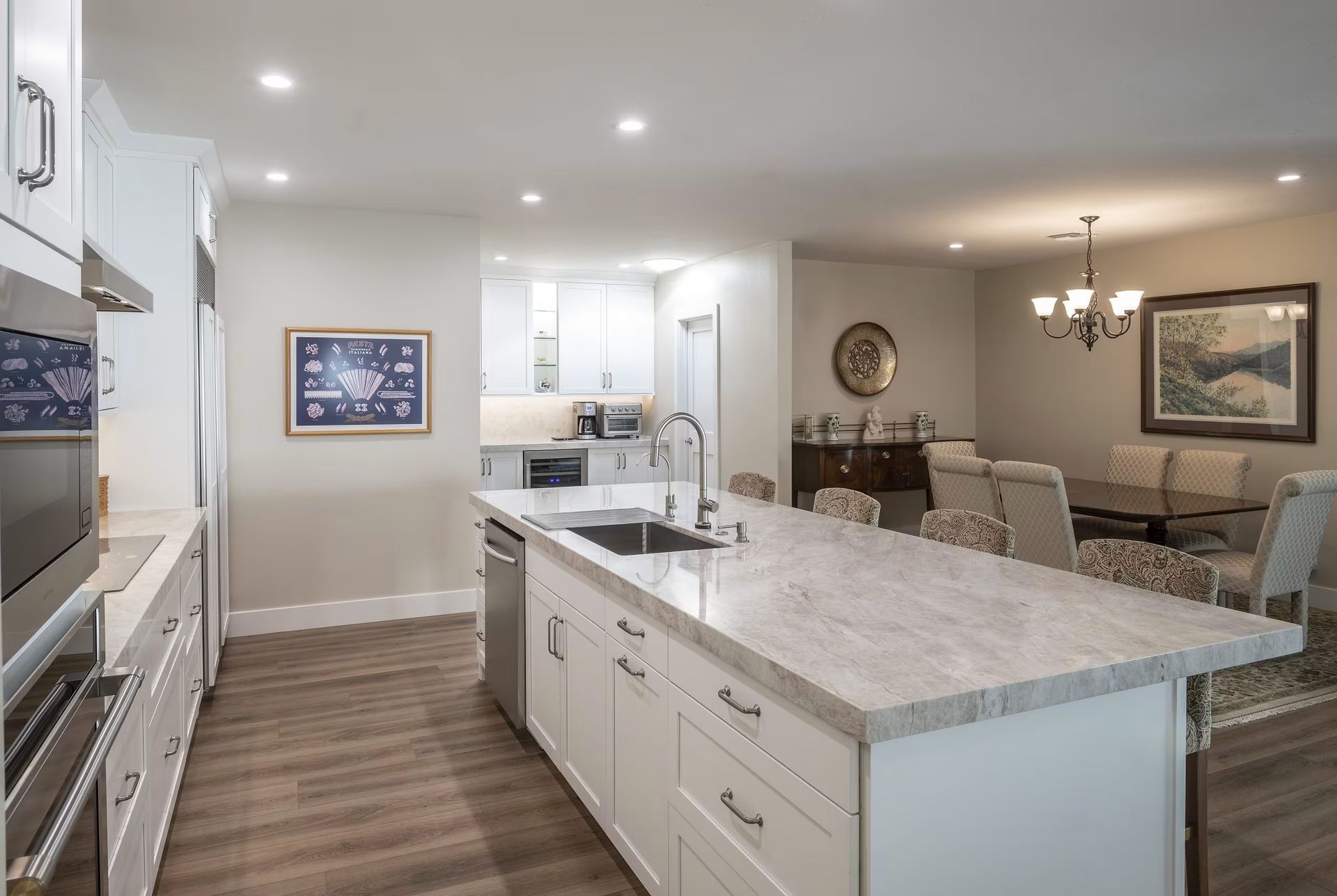 Modern open kitchen and dining area with white cabinetry, marble island, and wood-look flooring