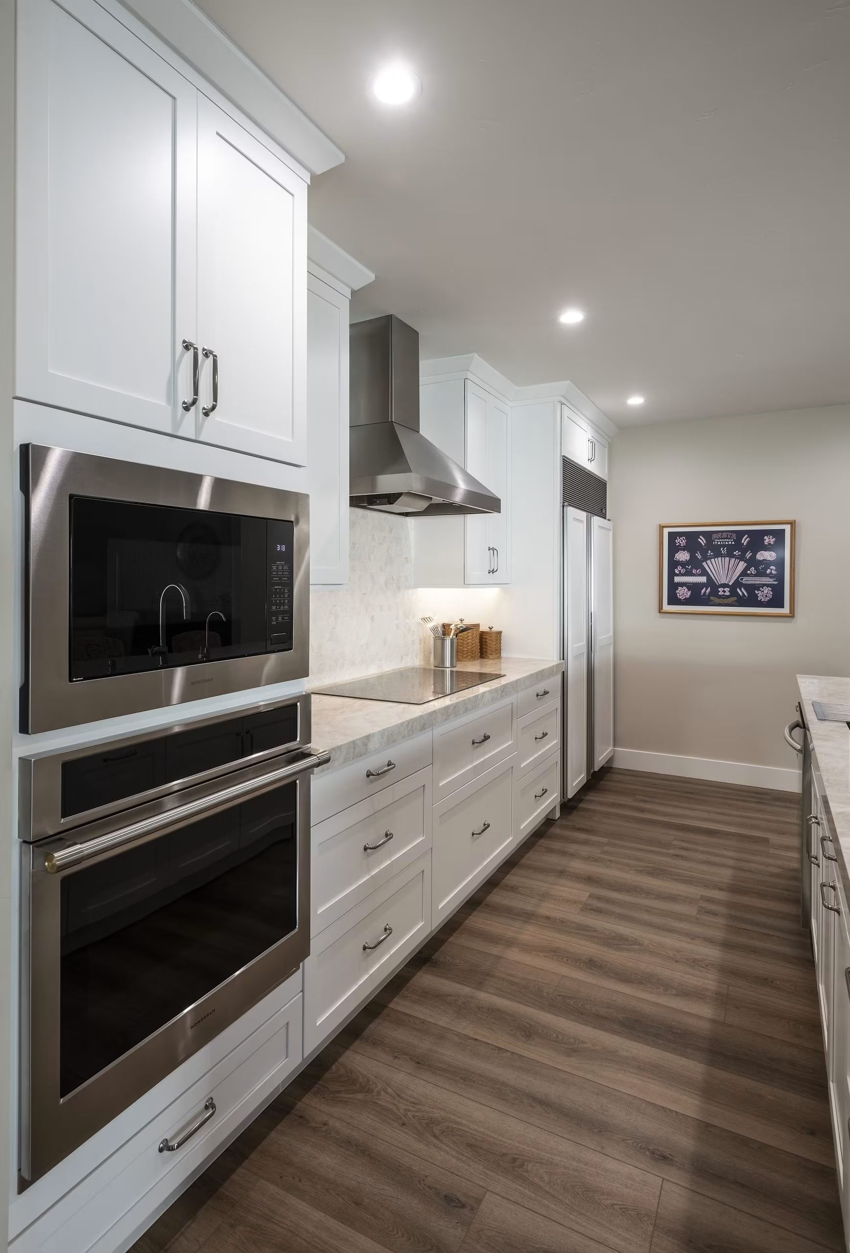 Bright white galley kitchen with built-in ovens, long counters, and wood-look flooring